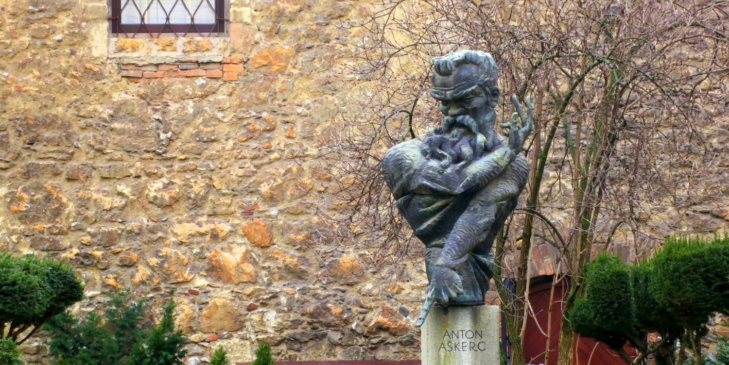 Na marmornem podstavku upodobljena bronasta poprsna plastika epskega pesnika, prevajalca in urednika Antona Aškerca. Spomenik je izdelal mozirski podobar Ciril Cesar, na zelenico pred mestno obzidje je bil postavljen leta 1963.